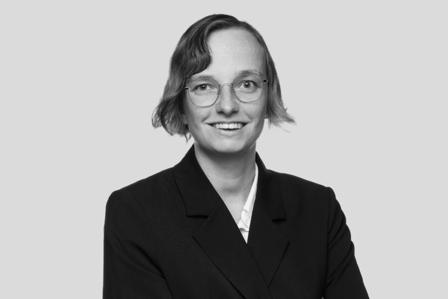 Eine Geschäftsfrau mit kurzen Haaren und einer Brille die in die Kamera lächelt.