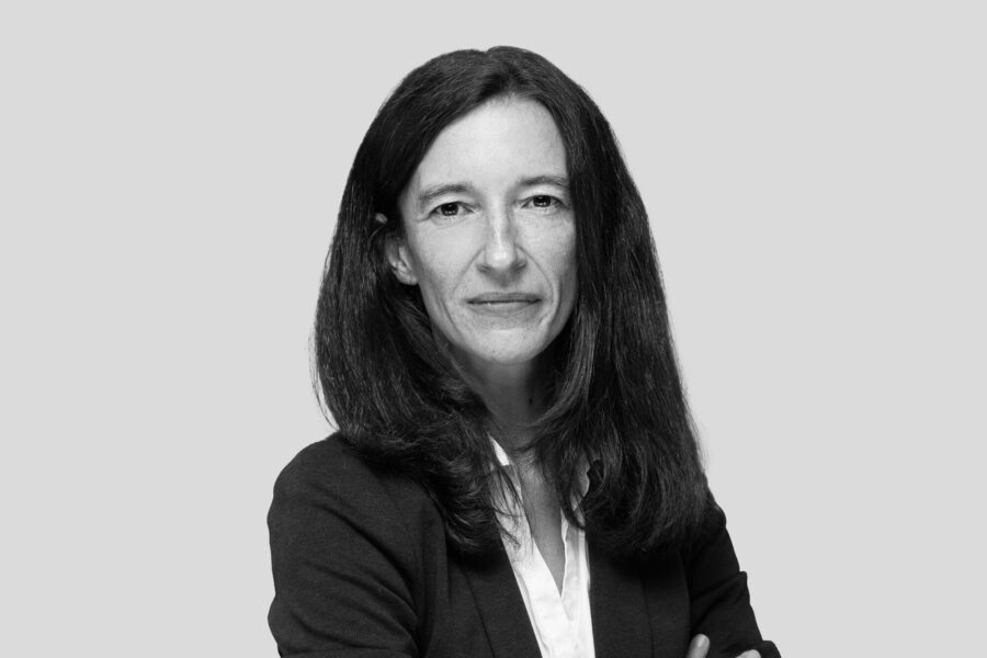 Eine Geschäftsfrau mit langen Haaren die in die Kamera lächelt.