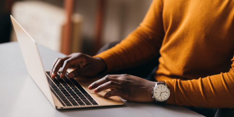 Mann sitzt am Laptop und schaut auf den Bildschirm. Er trägt eine Uhr an seiner linken Hand.